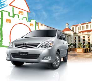 Silver Toyota Innova parked in front of a heritage building with a colorful mural of a fort in the background, illustrating car rental services from Udaipur to Jodhpur