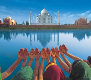 Tourists with raised hands in traditional attire facing the Taj Mahal reflected in water, illustrating popular Rajasthan tour packages.