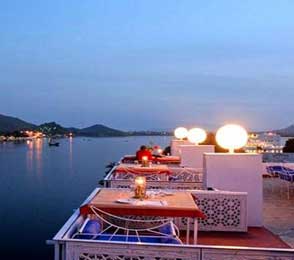 Evening view of a lakeside terrace dining area with tables set for guests, overlooking calm waters in Udaipur, illustrating private day tour experiences